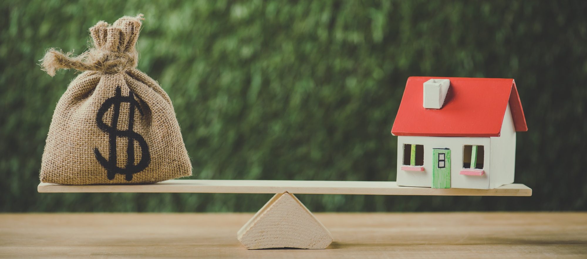 money bag with dollar symbol and house model balancing on swing on green background